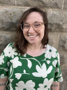 A white girl with brown hair and glasses wearing a green dress with white flowers.